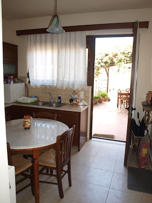 Una cocina con una mesa de comedor, sillas, un lavaplatos y una ventana con cortinas.
