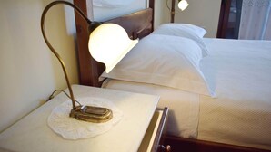 Una cama bien tendida con sábanas blancas, una lámpara de noche y un cabecero de madera.