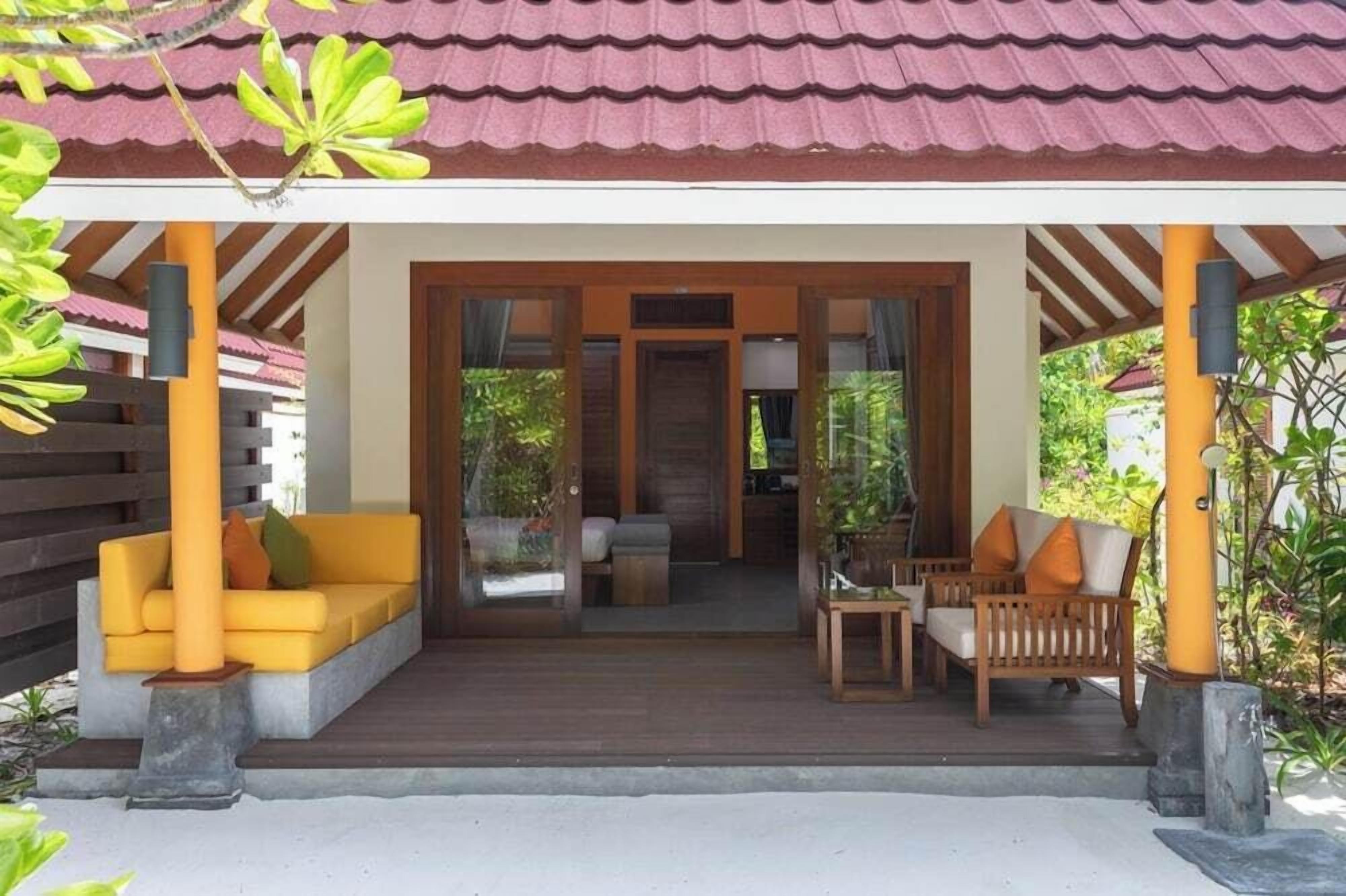 A covered outdoor seating area with a wooden bench and a yellow sofa.