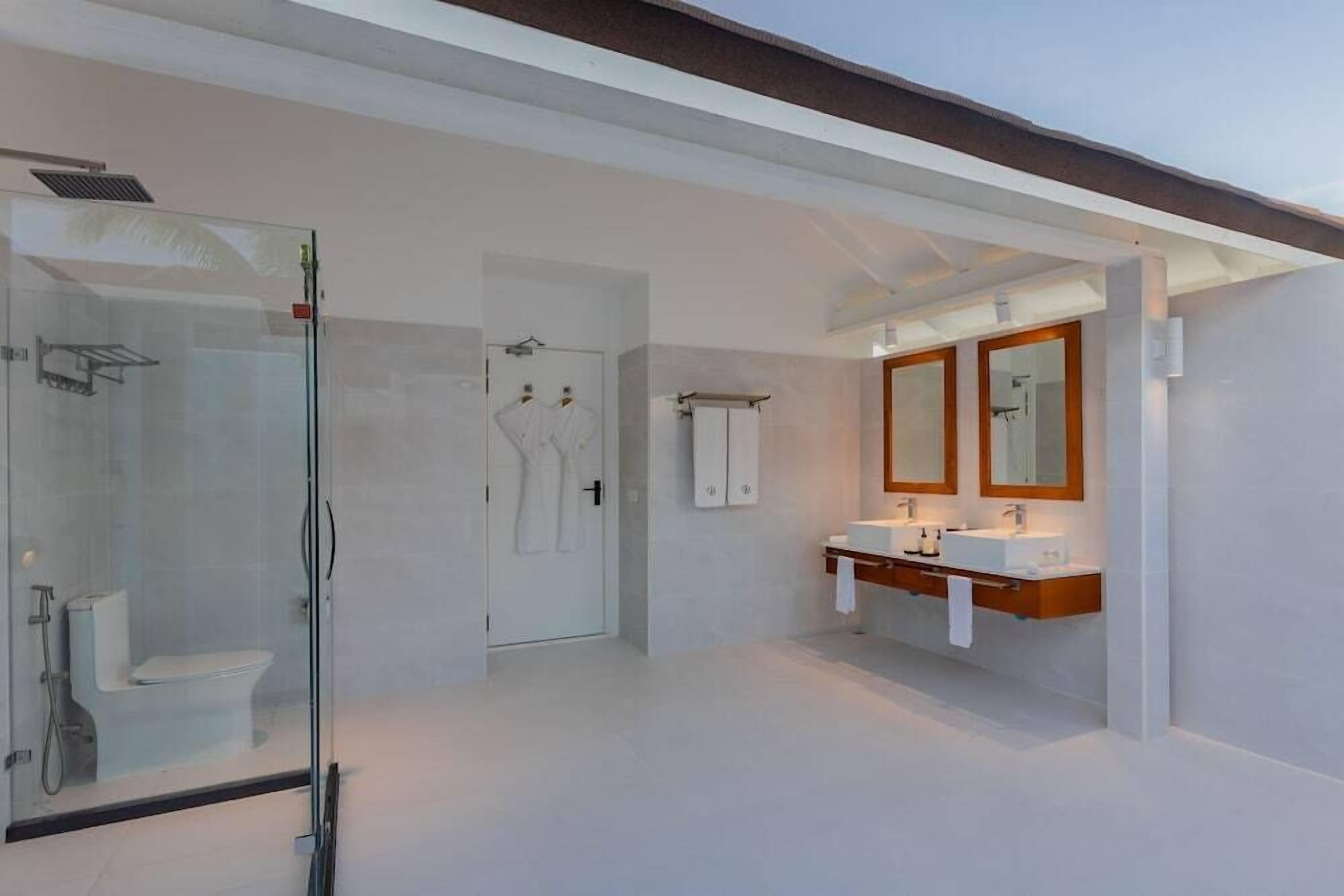 A modern bathroom with a glass-enclosed shower, a white toilet, and a vanity with two sinks and mirrors.