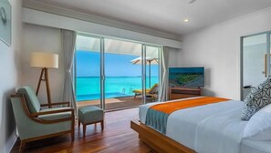Une chambre d’hôtel avec un lit, une chaise, une télévision et vue sur l’océan.