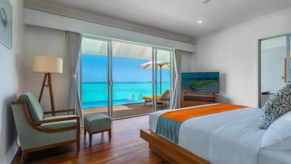 Une chambre d’hôtel avec un lit, une chaise, une télévision et vue sur l’océan.