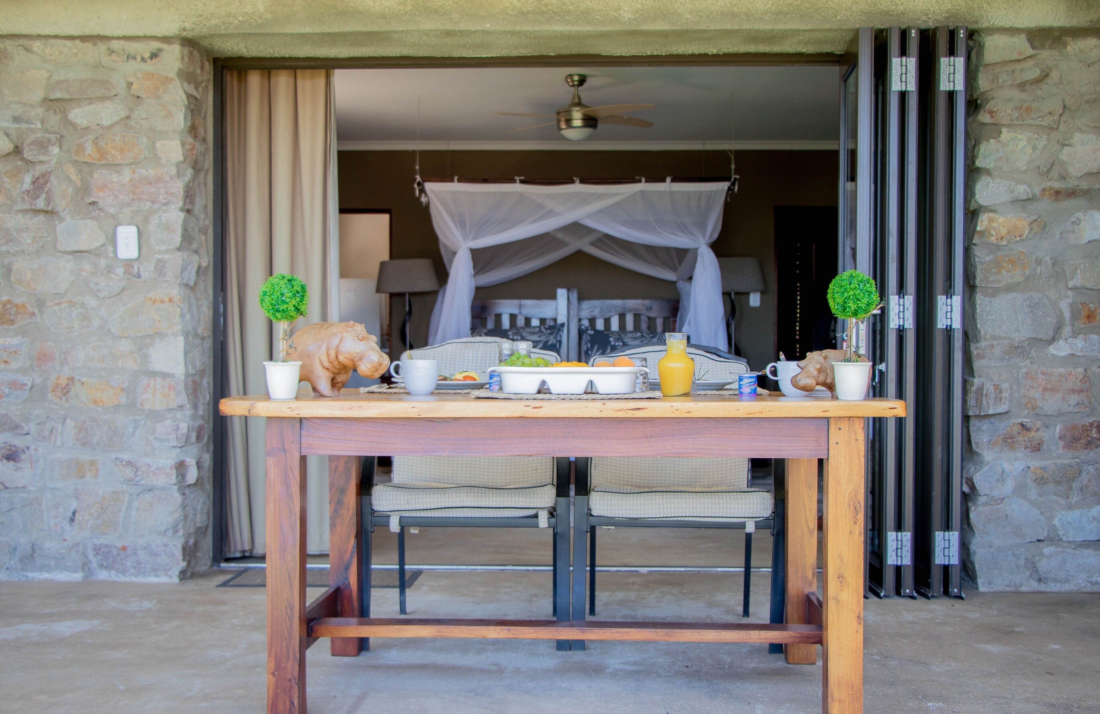 A dining table with food and drinks, set against a stone wall with a canopy.