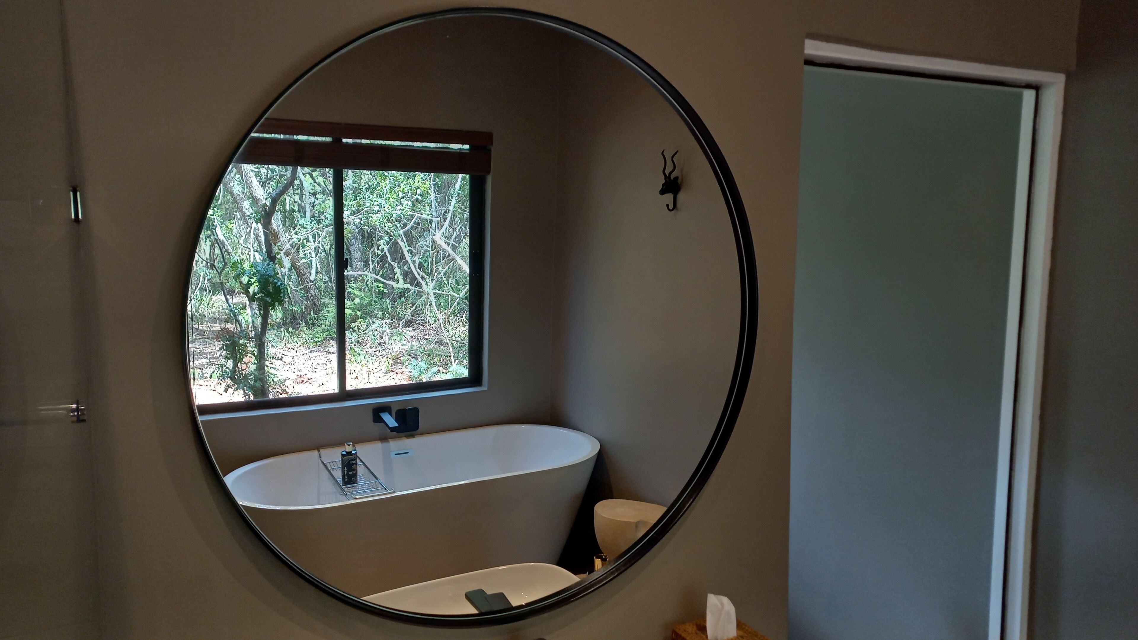 Un baño con un espejo redondo, una bañera y un ventanal.