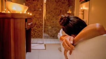 A person leaning on a wall with a candle on a wooden table.