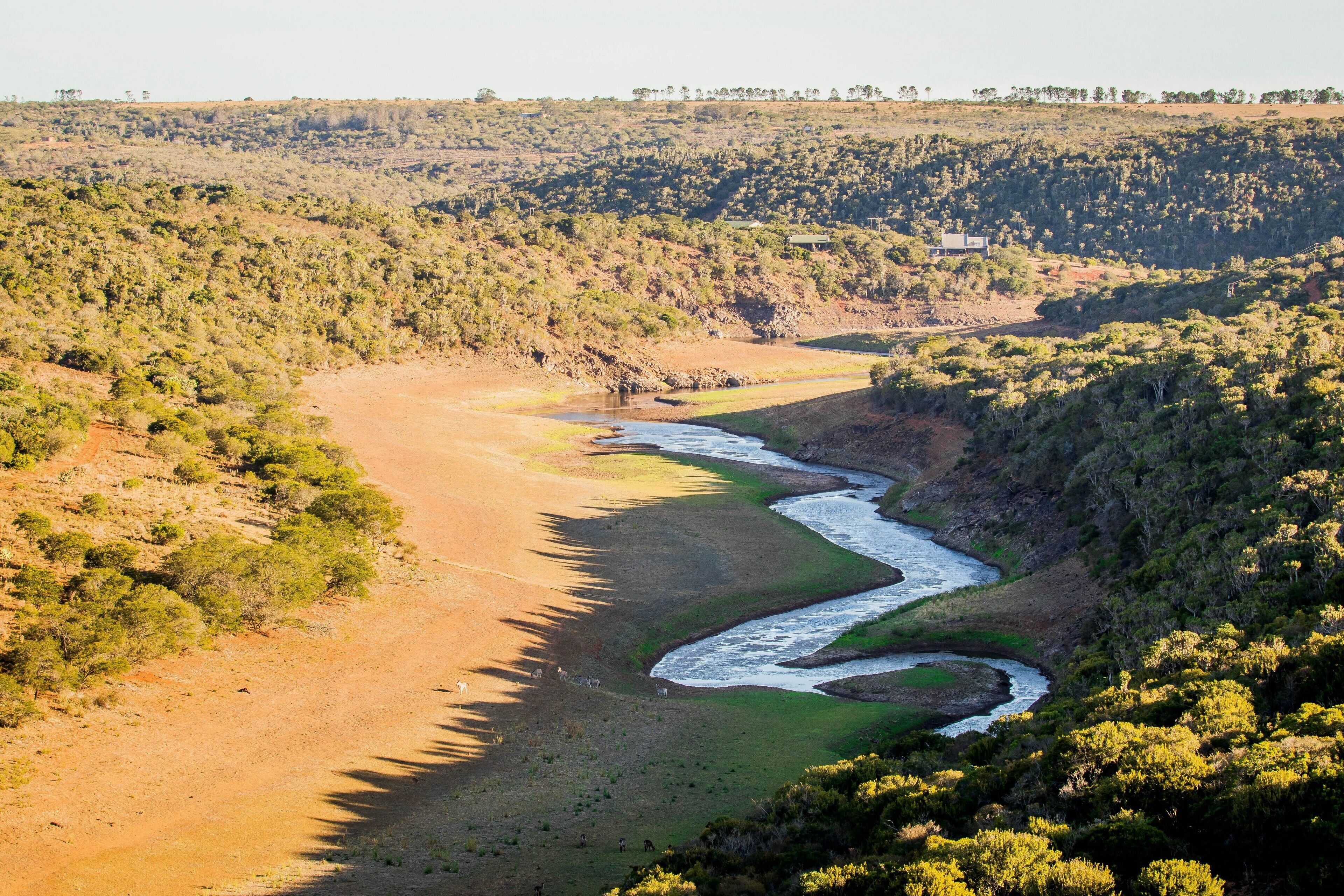 A river winding through a hilly landscape with sparse vegetation and a few scattered buildings.