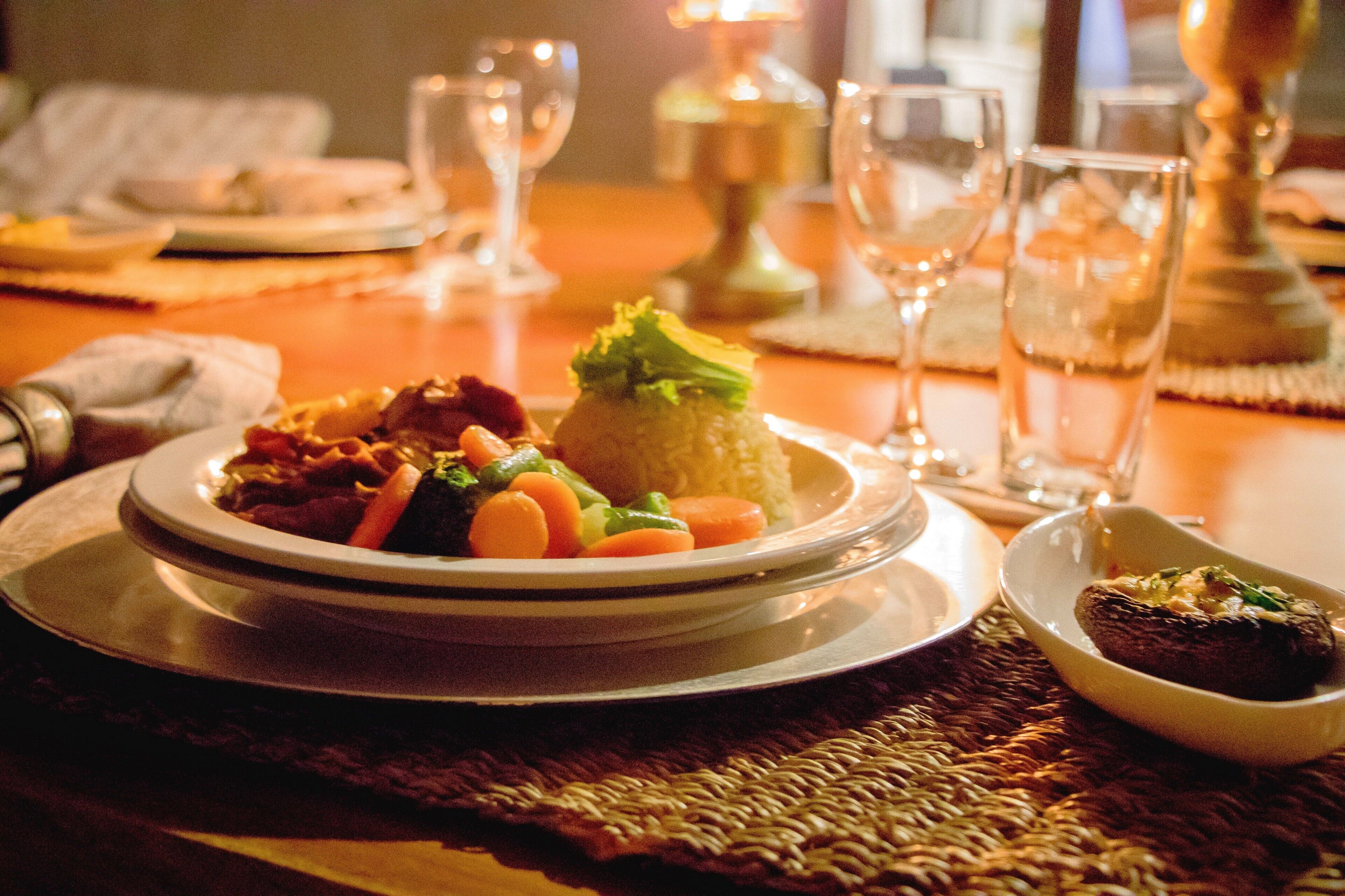 Une table à manger dressée avec des assiettes remplies de nourriture, des verres et une bougie.