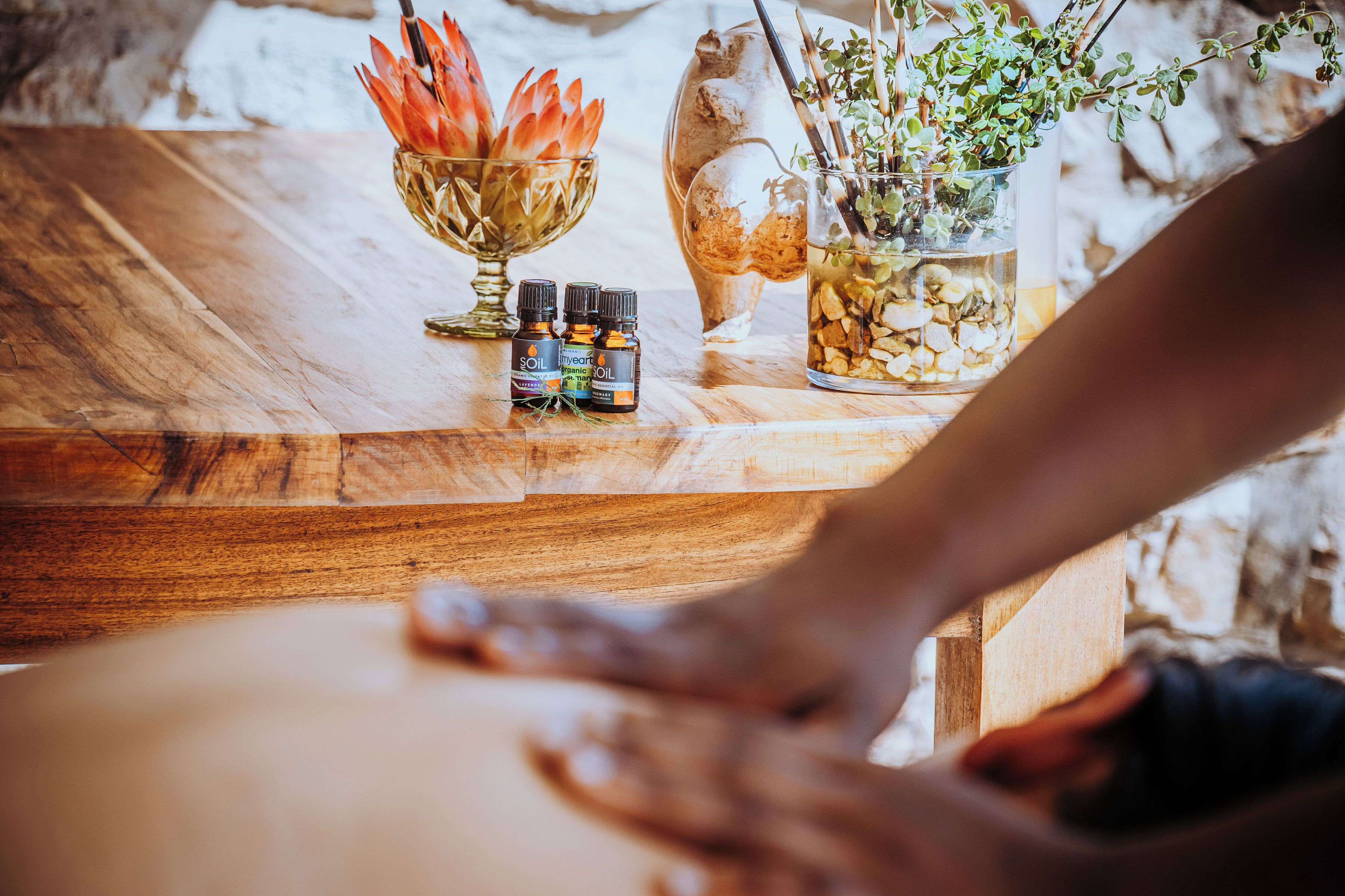 Una mesa de madera con un cuenco de vidrio con flores secas, un tarro de cristal con una planta y dos pequeñas botellas de aceites esenciales.