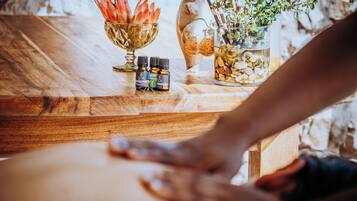 Una mesa de madera con un cuenco de vidrio con flores secas, un tarro de cristal con una planta y dos pequeñas botellas de aceites esenciales.