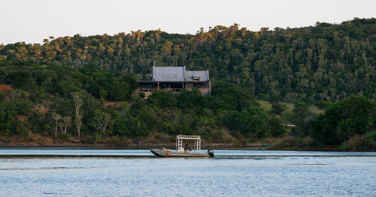 A house on a hill with a boat on the water in front.