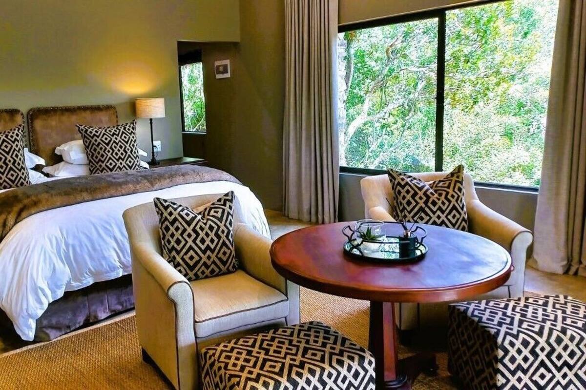 A hotel room with a large bed, two bedside tables with lamps, a round table with a vase, and patterned cushions.