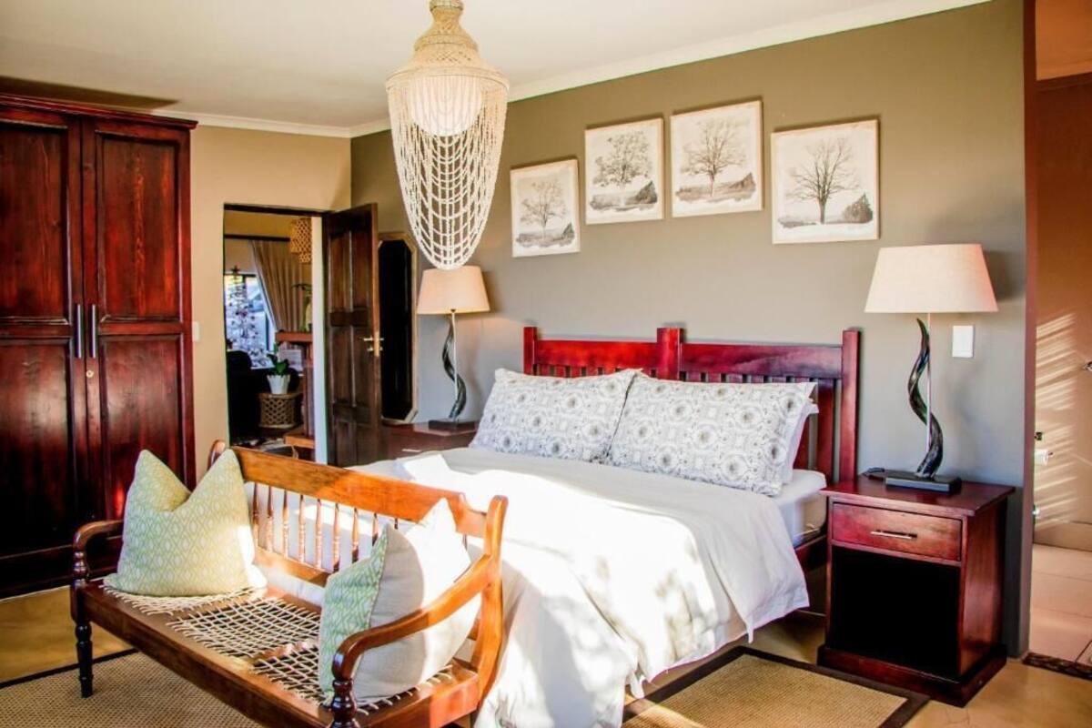 A bedroom with a wooden bed, two bedside lamps, a bench with cushions, and a chandelier.
