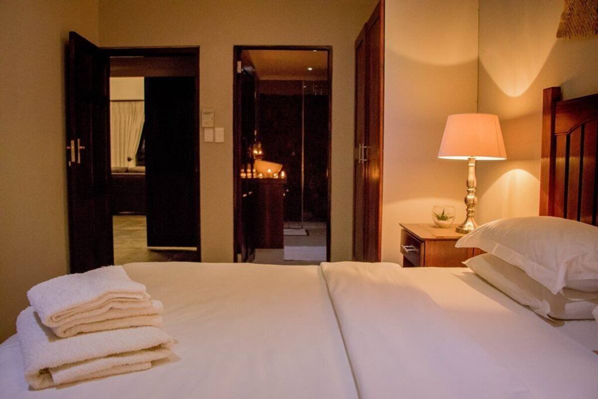 A hotel room with a neatly made bed, a bedside lamp, and a stack of towels.