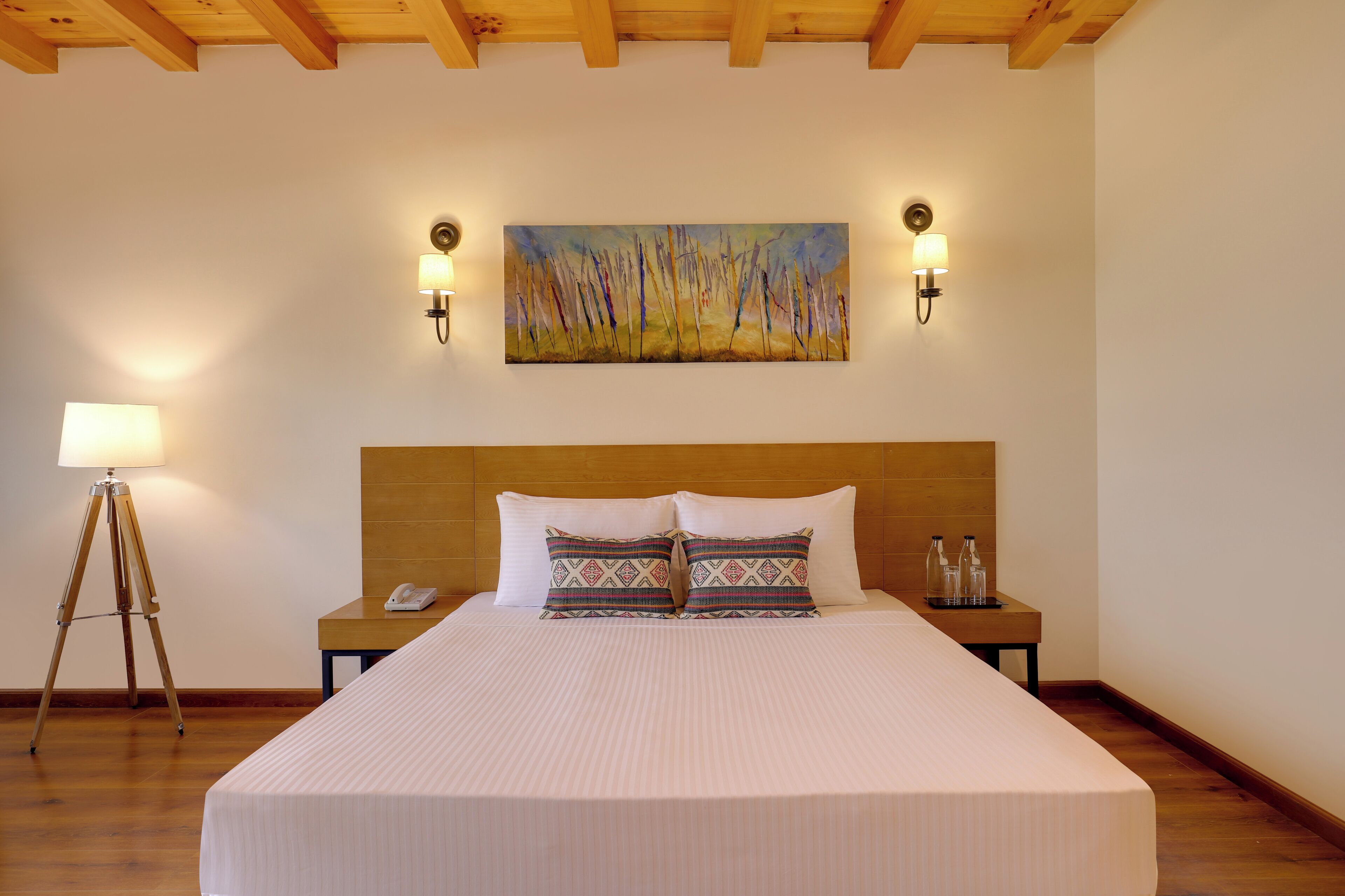 Camera d'albergo con un letto grande, due comodini, una lampada, un quadro appeso e un soffitto in legno.