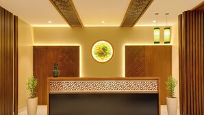 A reception desk with a logo, two potted plants, and a patterned wall design.