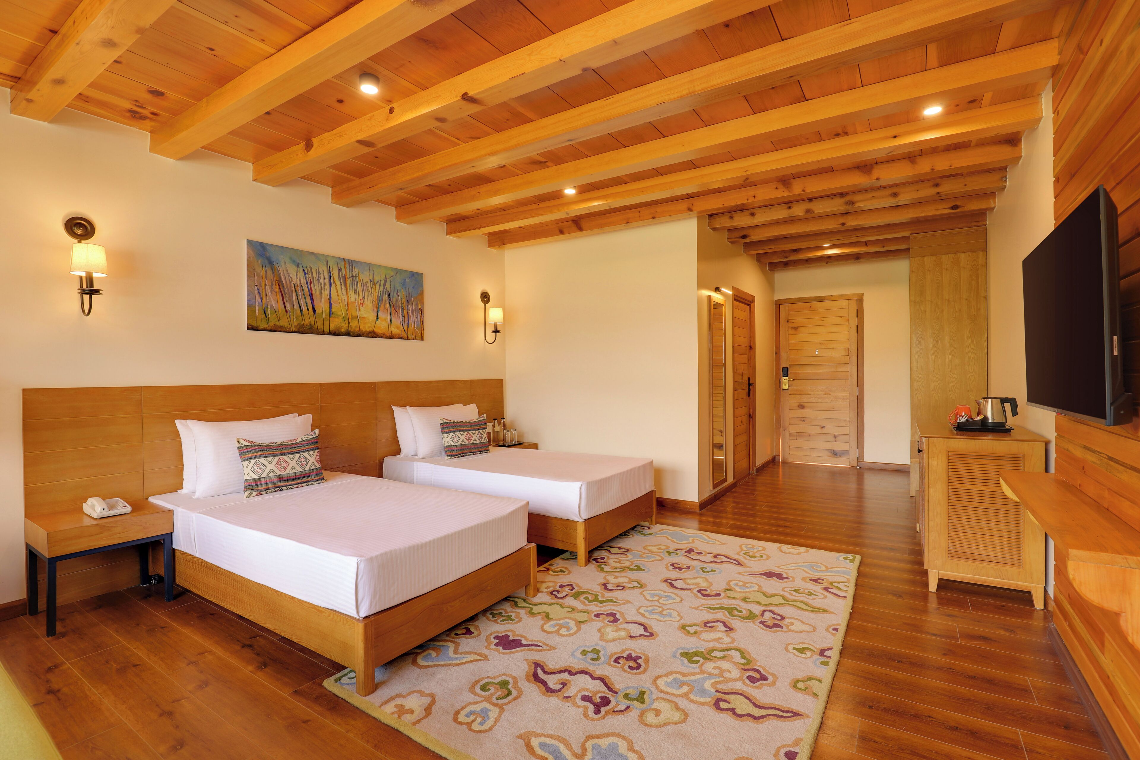 Habitación de hotel con dos camas, vigas de madera en el techo y un cuadro en la pared, además de un televisor a la derecha.