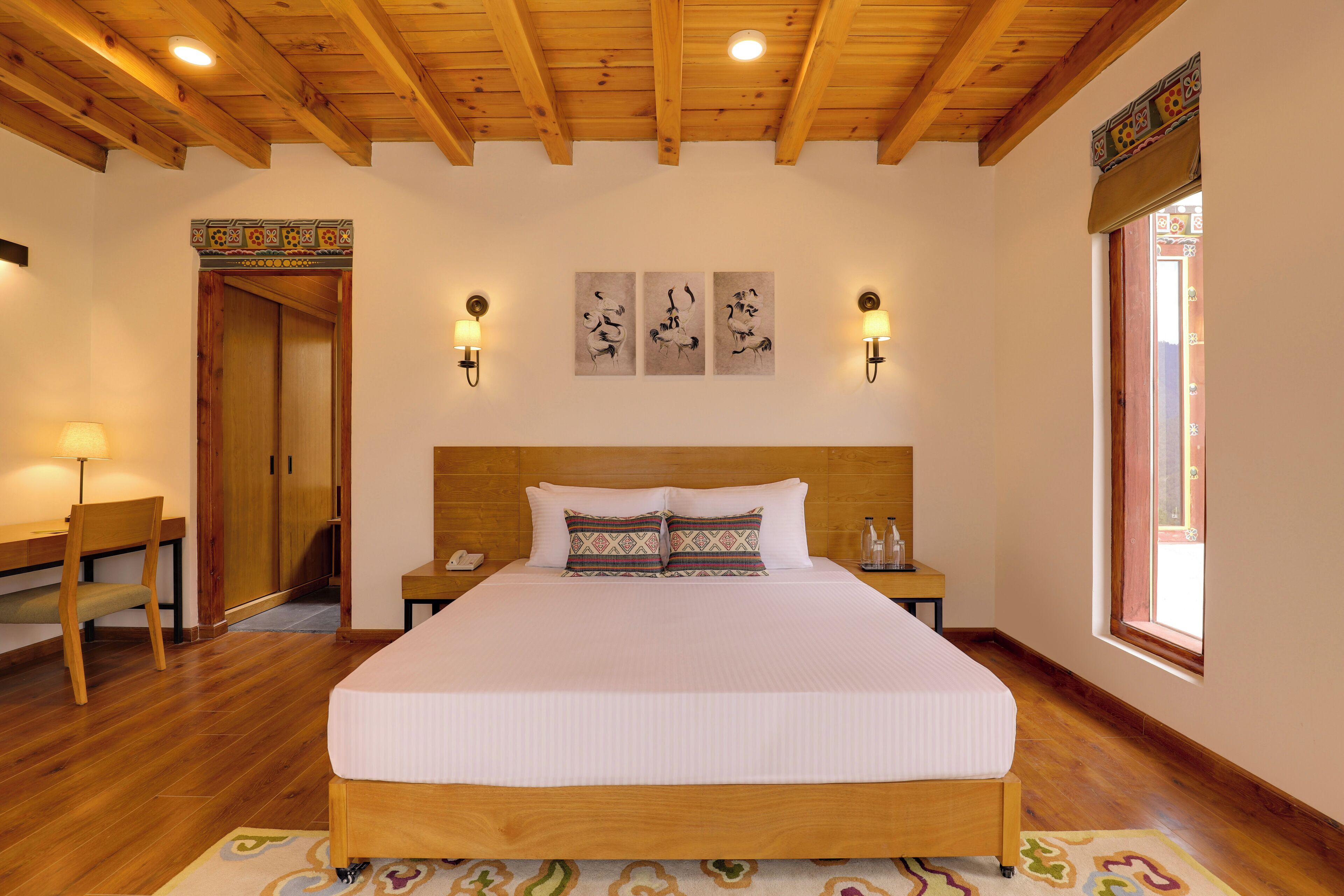 A bedroom with a wooden bed, two bedside tables, a desk, a chair, and a window.