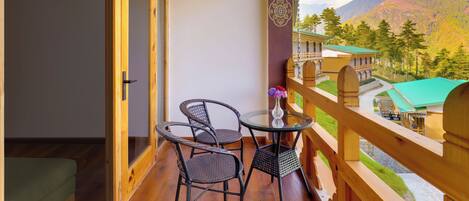 A balcony with wicker chairs and a table, overlooking a mountainous landscape with a building in the background.