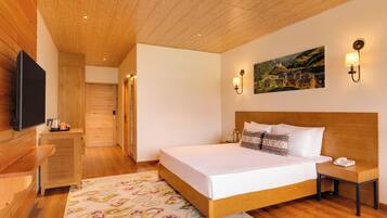 A bedroom with a wooden ceiling, a bed with white linens, a nightstand, a wall-mounted TV, and a painting of a village.