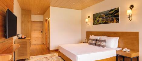 A bedroom with a wooden ceiling, a bed with white linens, a nightstand, a wall-mounted TV, and a painting of a village.