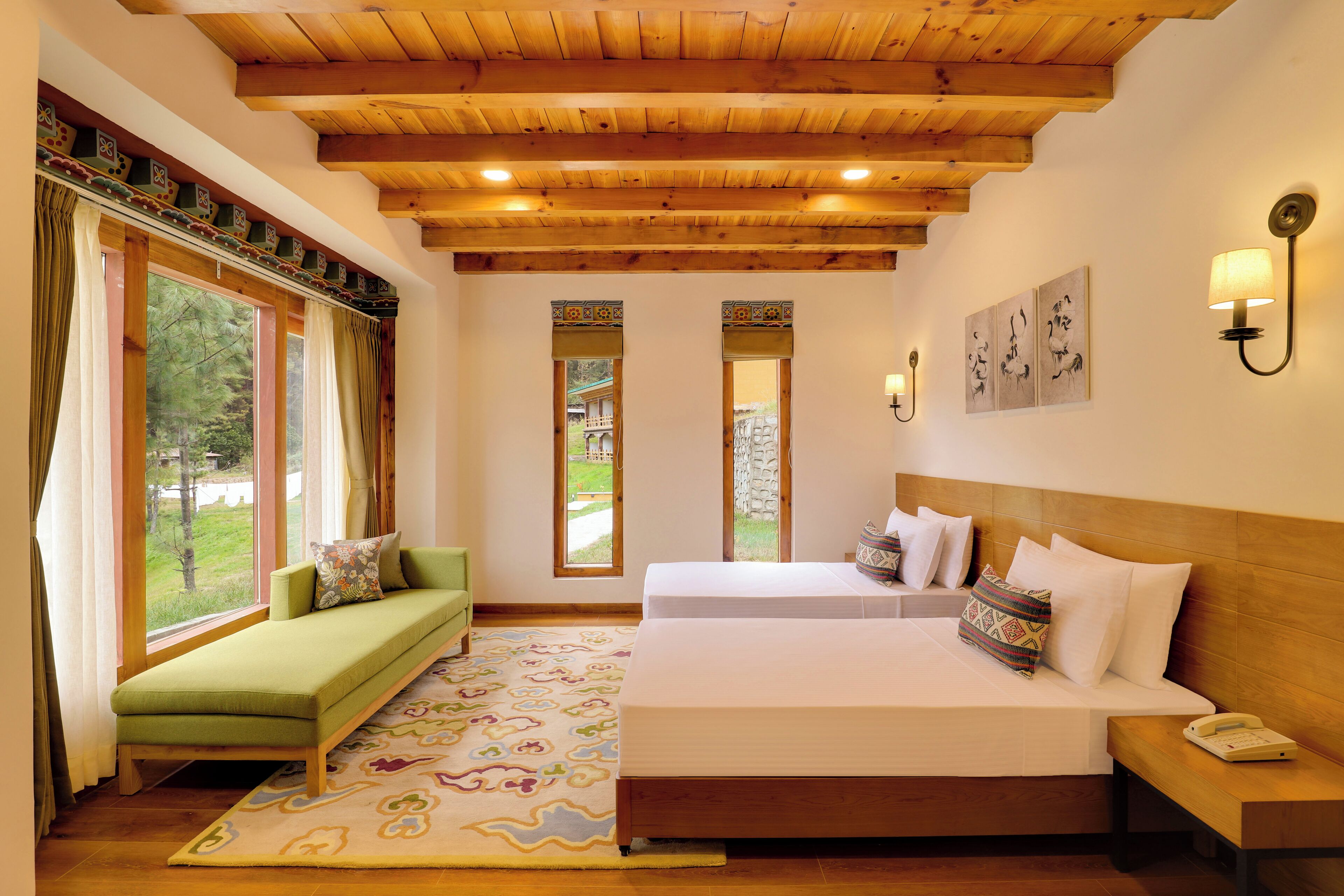 A room with a wooden ceiling, a sofa, a bed with two pillows, a bedside table with a phone, and a window with curtains.