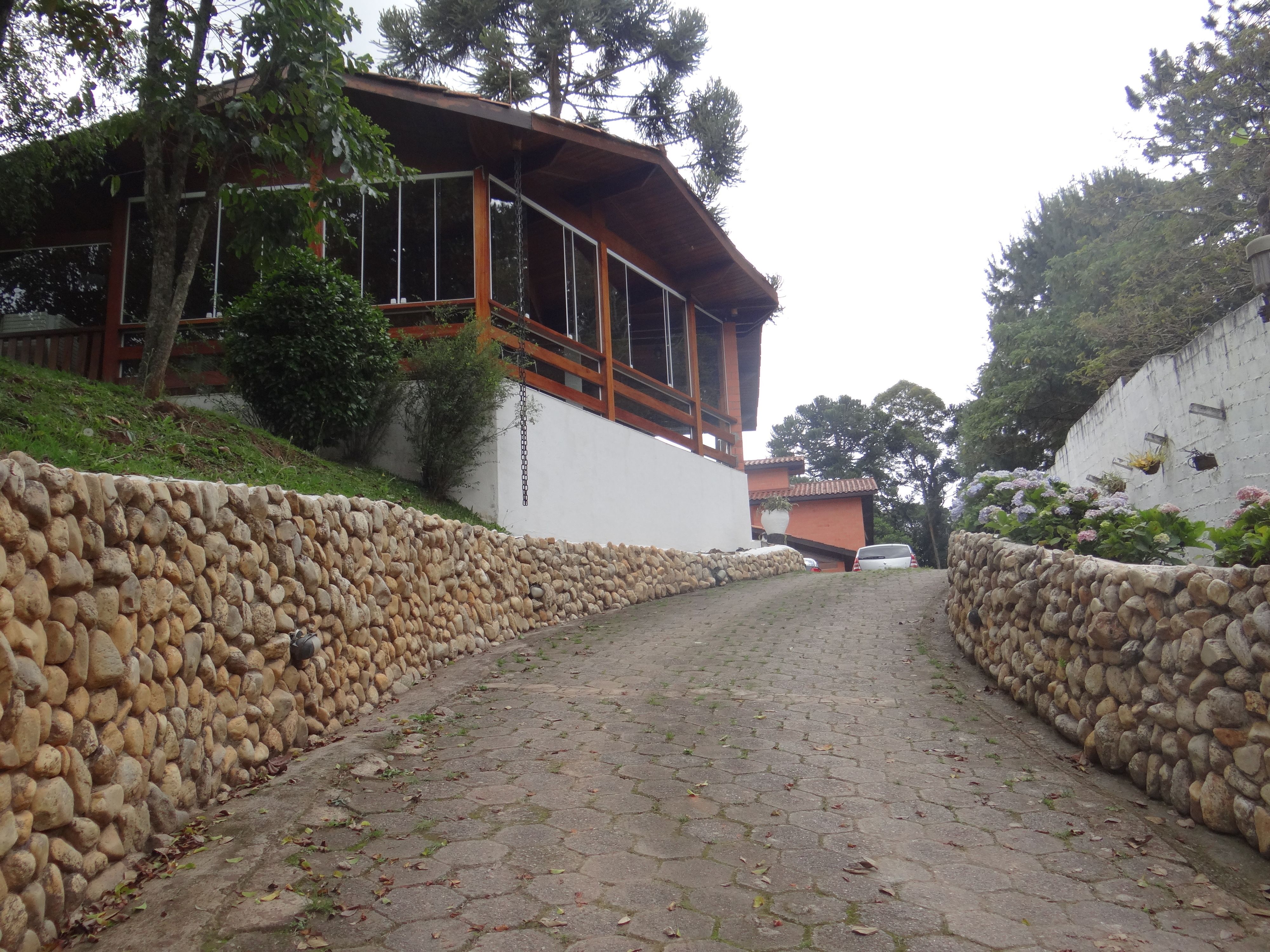 A stone pathway leading to a building with a wooden balcony and a white wall.