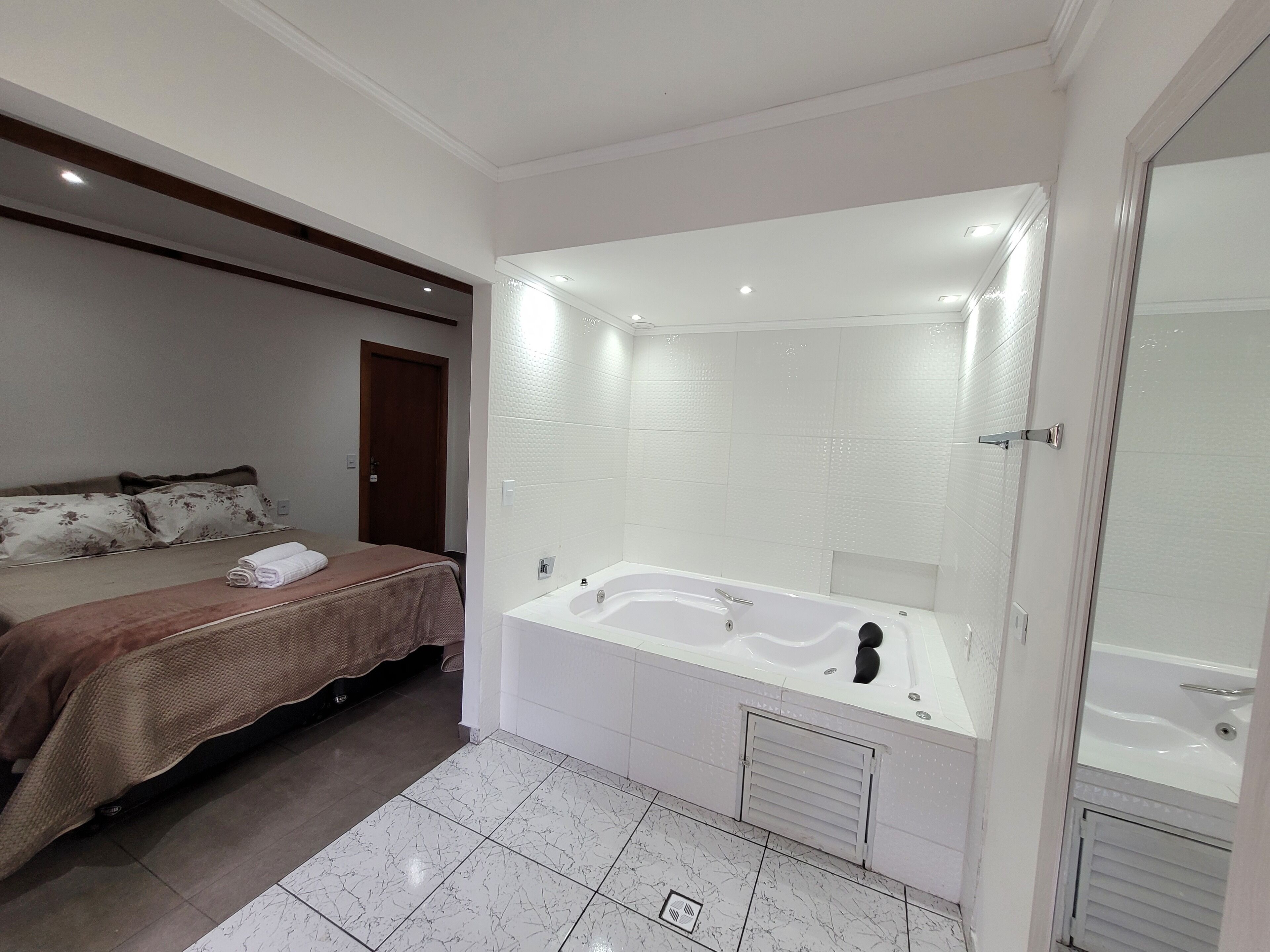 Quarto moderno com uma cama grande, banheiro separado com banheira e área de chuveiro.