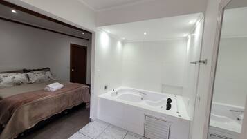 Quarto moderno com uma cama grande, banheiro separado com banheira e área de chuveiro.