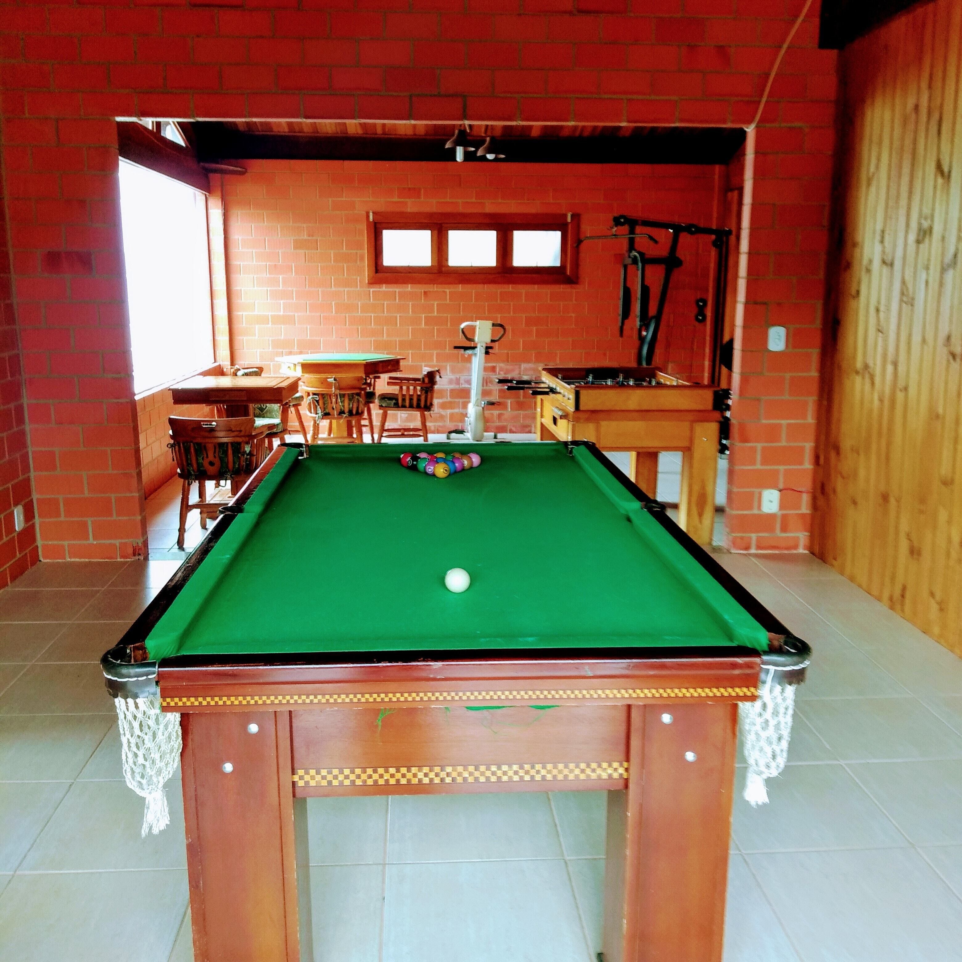 A pool table in a room with brick walls, a wooden table, and chairs.