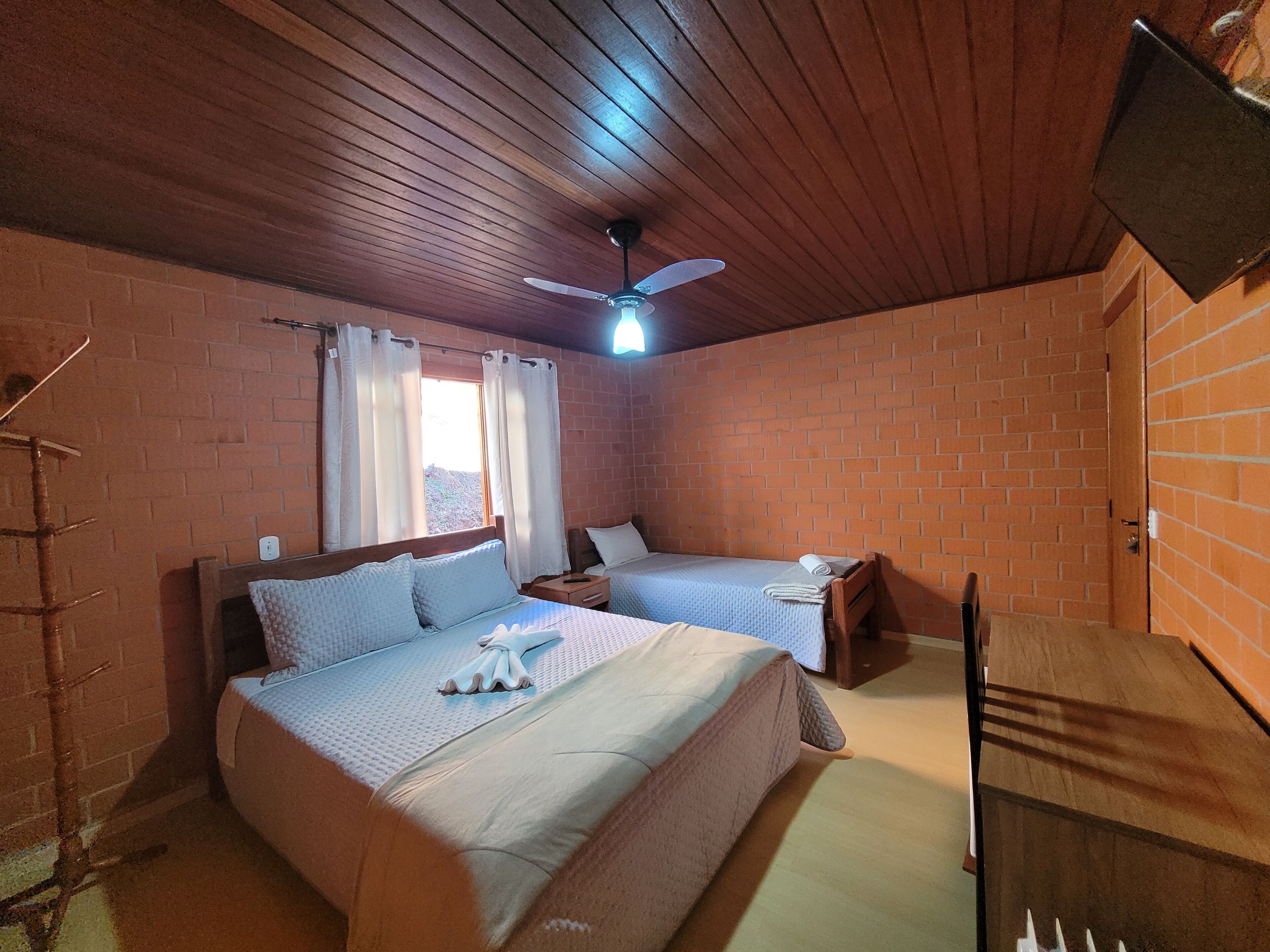 Een kamer met twee bedden, een plafondventilator en bakstenen muren.