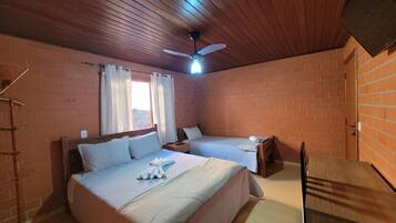 A room with two beds, a ceiling fan, and brick walls.