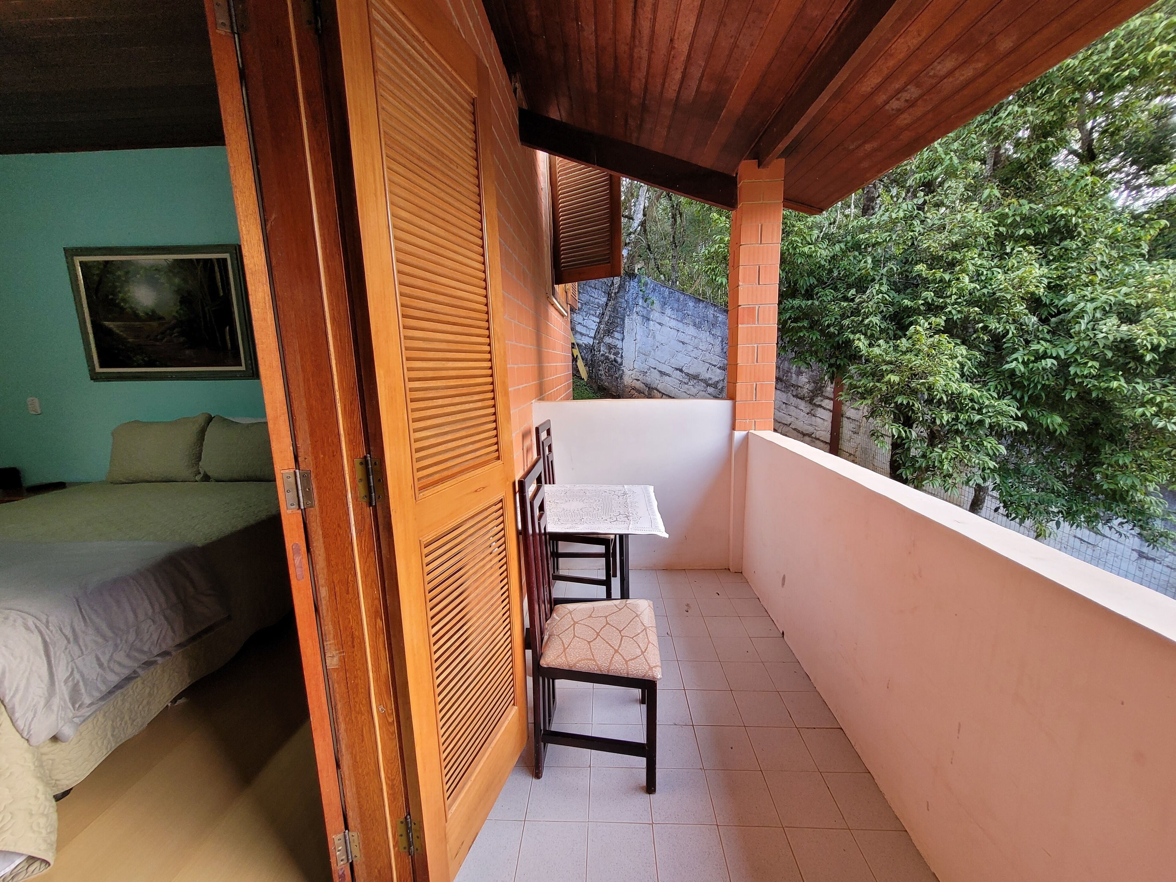 A balcony with a table and chairs, a bed with a view, and a wooden door.
