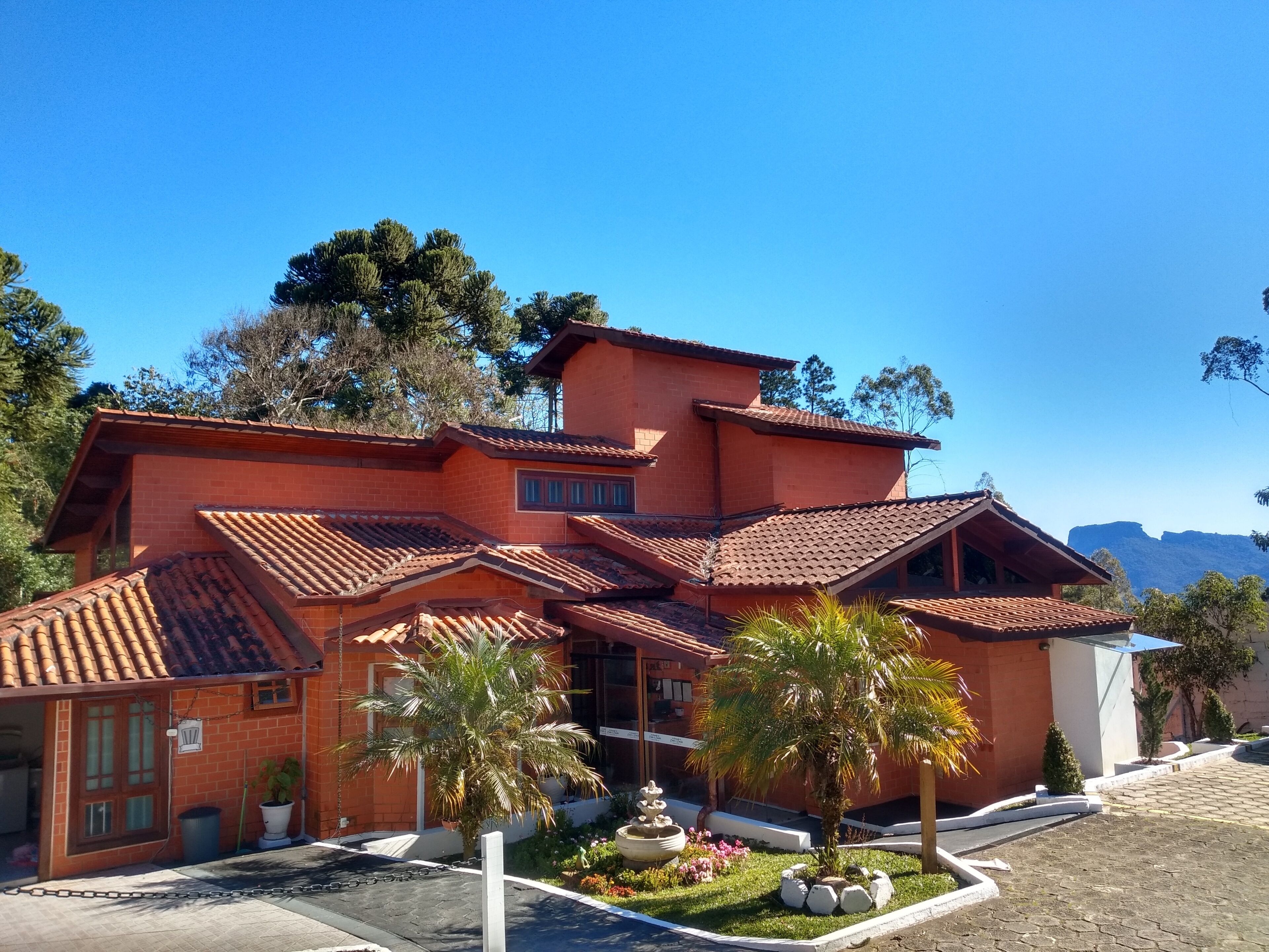 A multi-story building with a red brick facade, terracotta roof tiles, and a landscaped front yard with palm trees and a fountain.