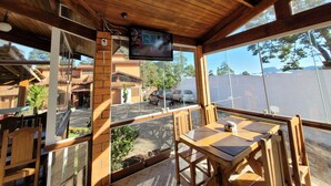 Una habitación con paneles de madera, un televisor montado en la pared, una mesa con sillas y amplias ventanas que dan al área de estacionamiento y edificios exteriores.