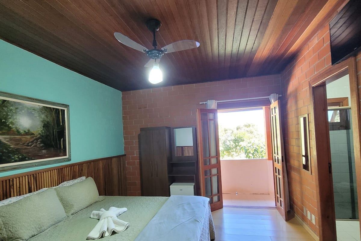 A bedroom with a wooden ceiling, a bed with a white bedspread, a ceiling fan, and a painting on the wall.