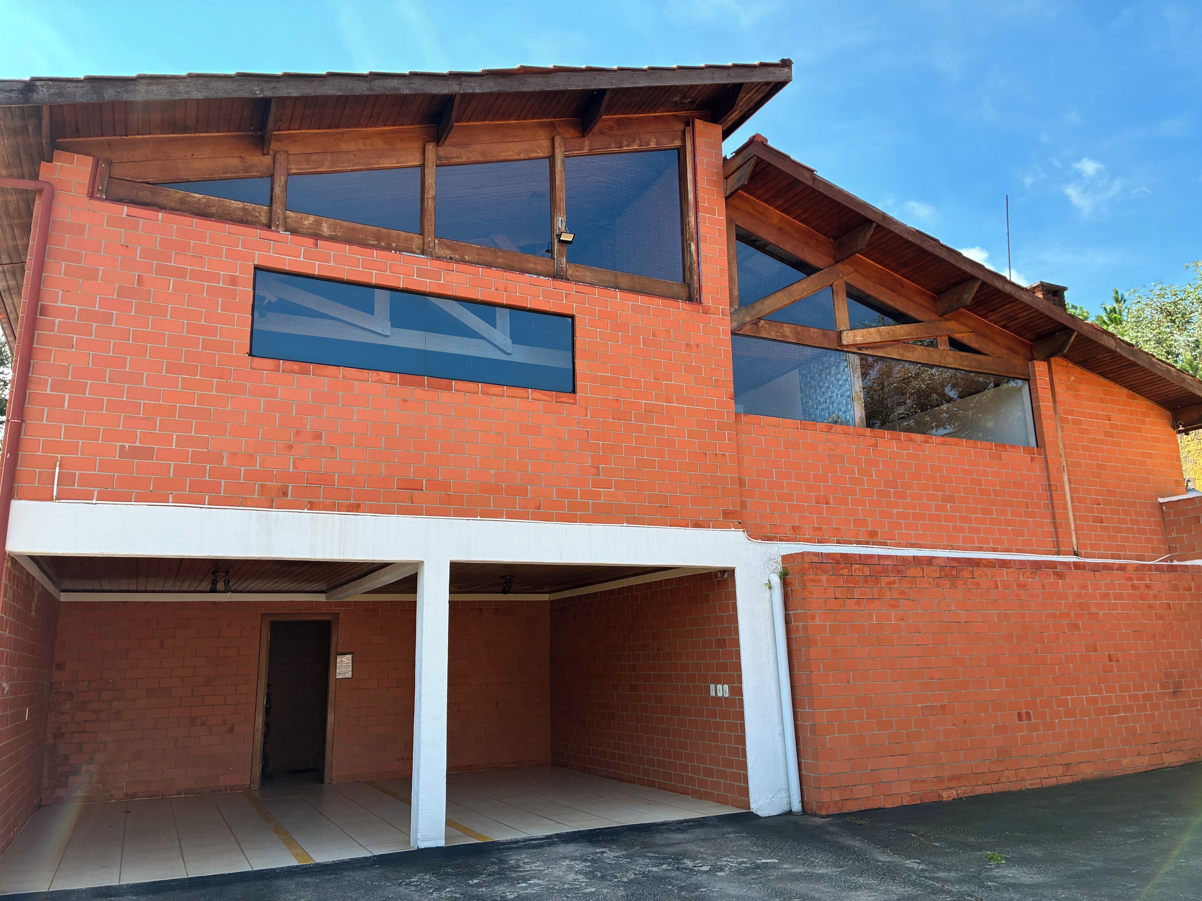 Un edificio de dos pisos con fachada de ladrillo, ventanas amplias y un área de estacionamiento techada.