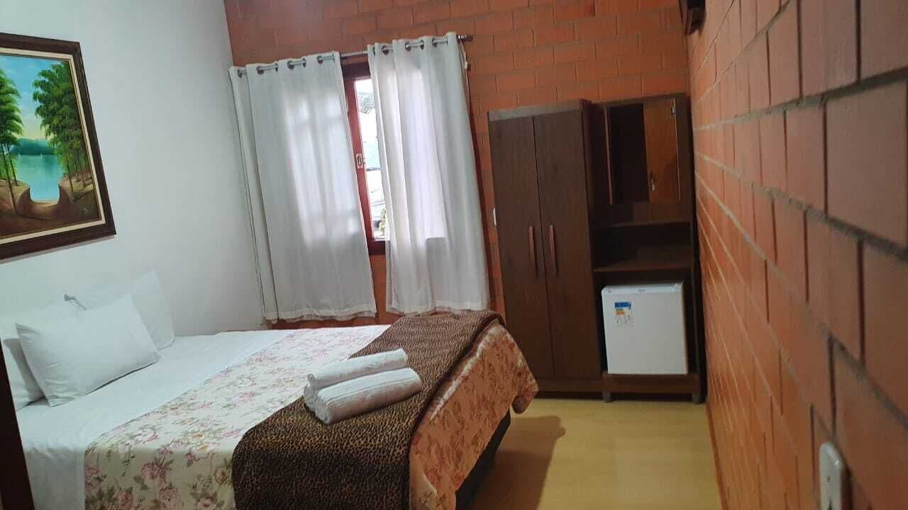 A bedroom with a bed, a desk, a wardrobe, and a small refrigerator.