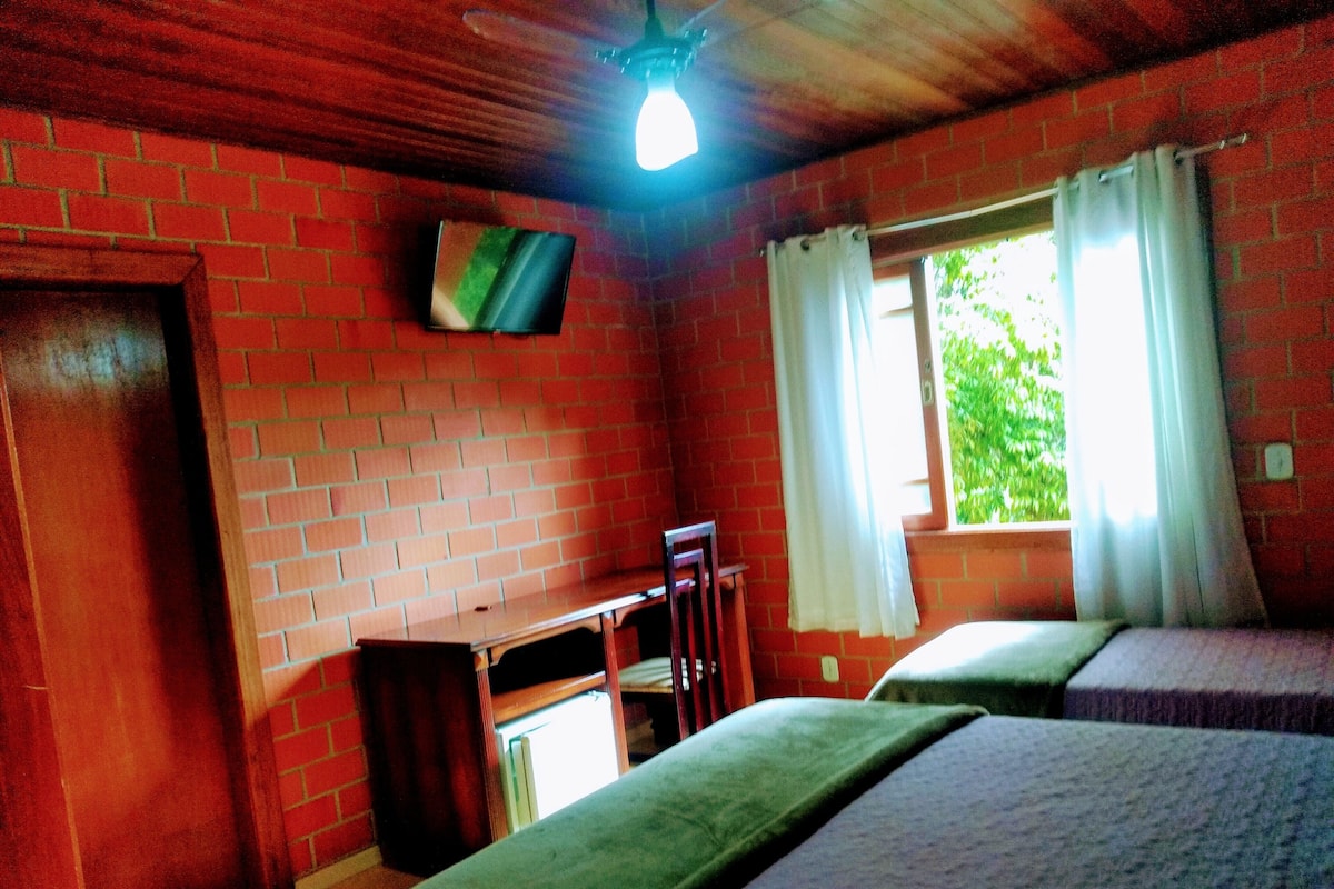 A room with brick walls, a wooden ceiling, a desk, two beds, and a window with curtains.