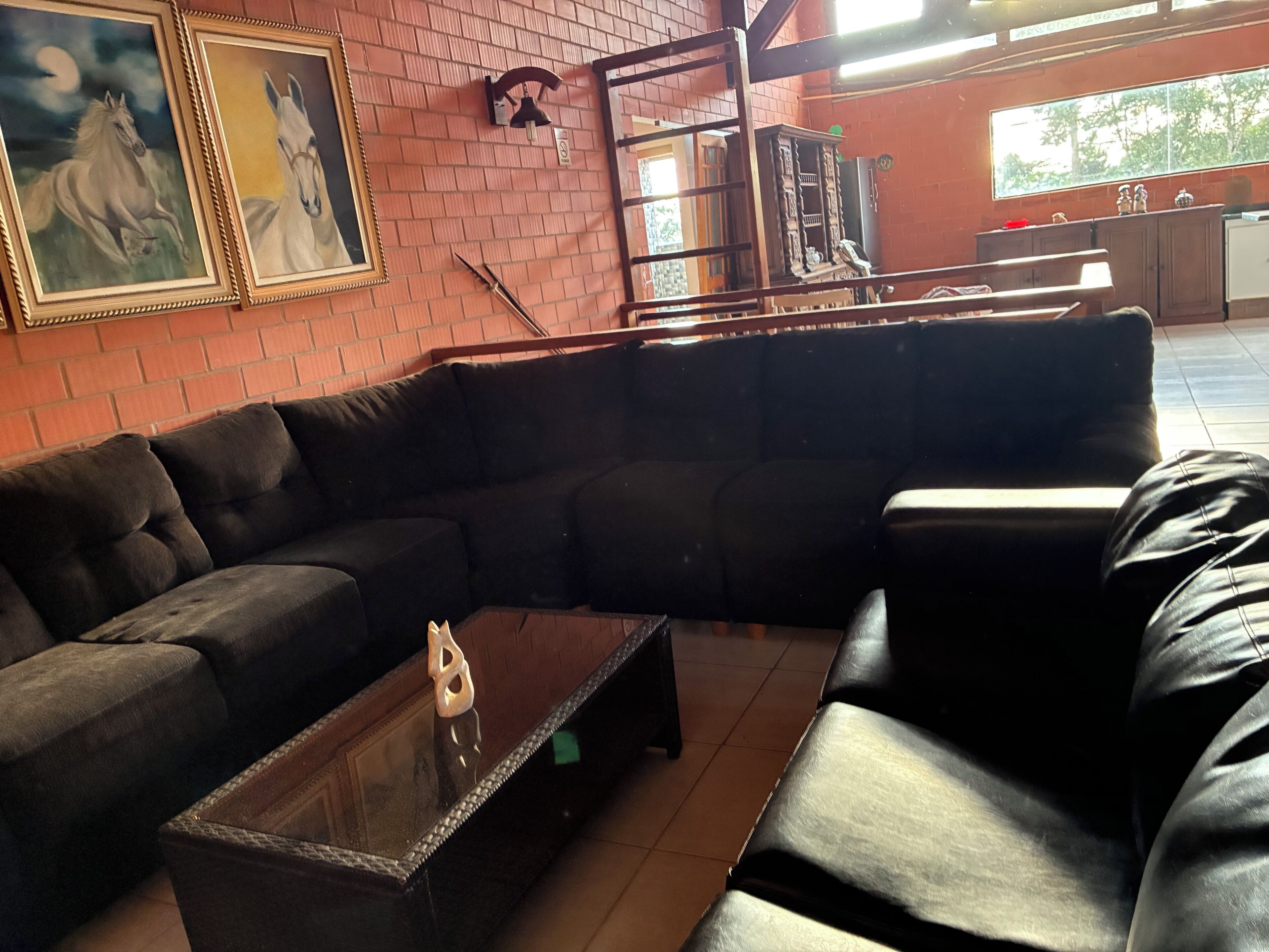 Una sala de estar moderna con un sofá modular, una mesa de centro de vidrio y dos cuadros enmarcados con caballos en la pared.