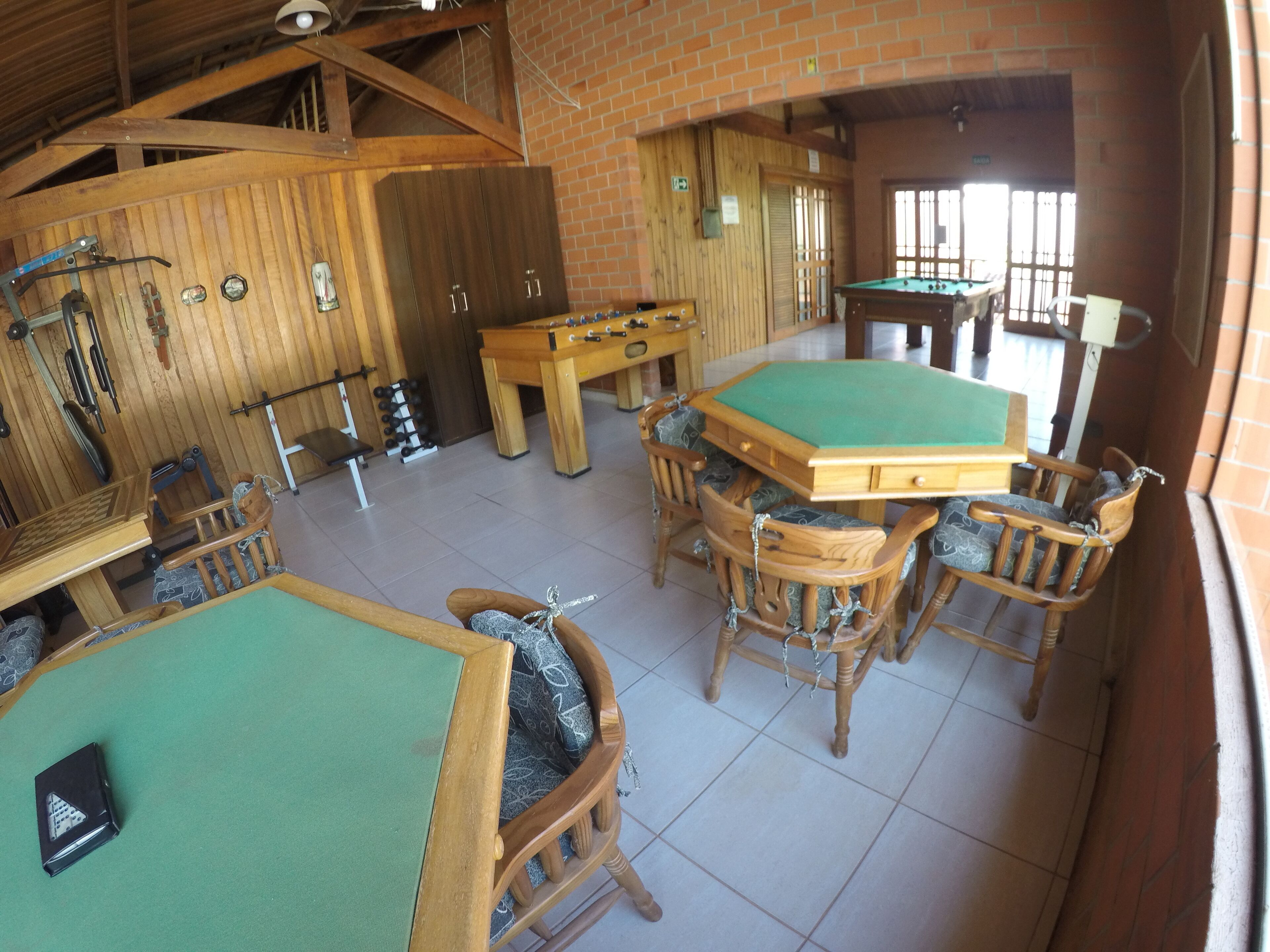 Uma sala de bilhar com várias mesas e cadeiras, paredes de madeira e teto alto.