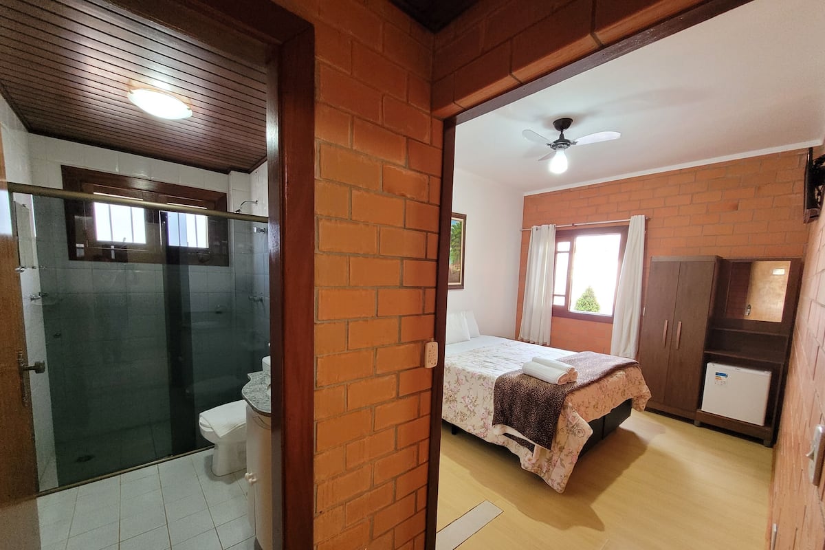 A room with a shower, a bed with a floral bedspread, a wardrobe, and a ceiling fan.