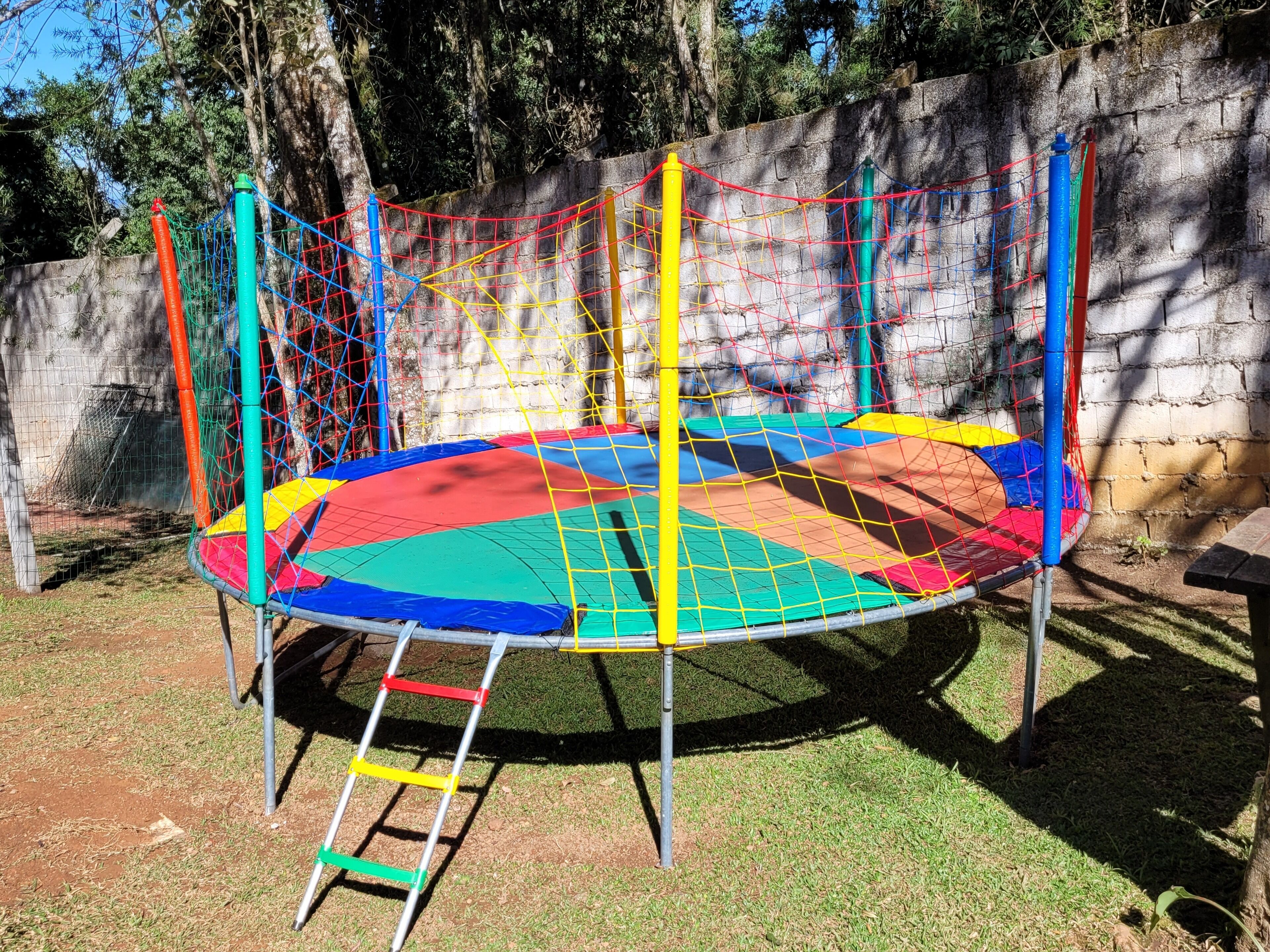Un trampolín con red de seguridad, rodeado de un muro de piedra y árboles.