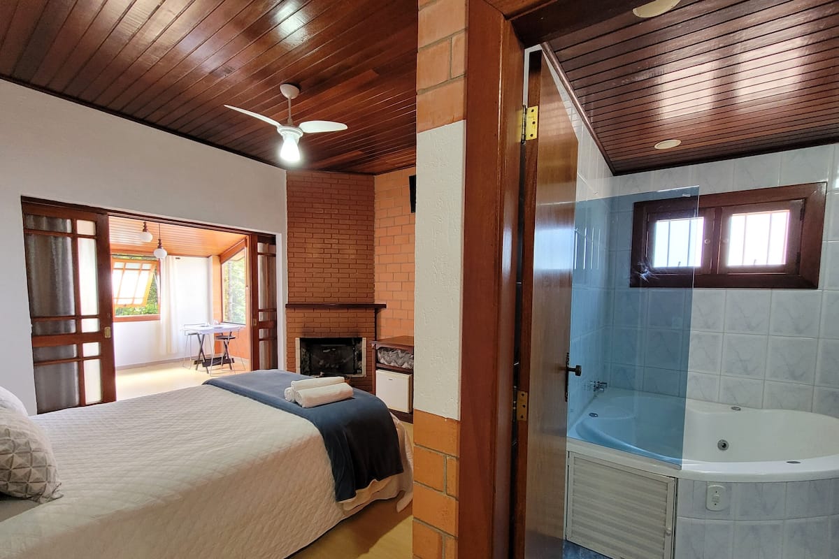 A bedroom with a bed, a fireplace, and a bathroom with a bathtub.