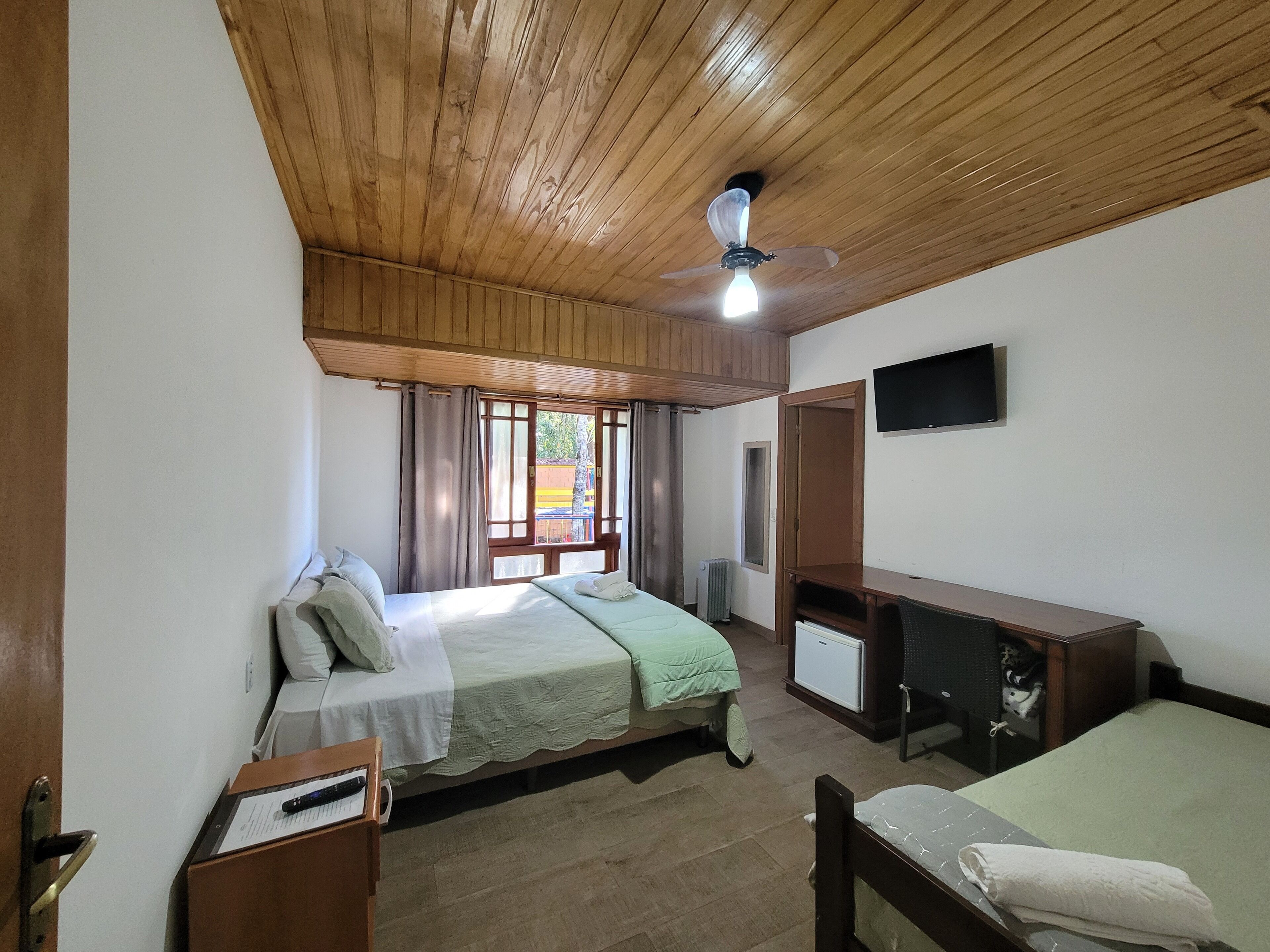 Een kamer met een bed, bureau, televisie en plafondventilator.