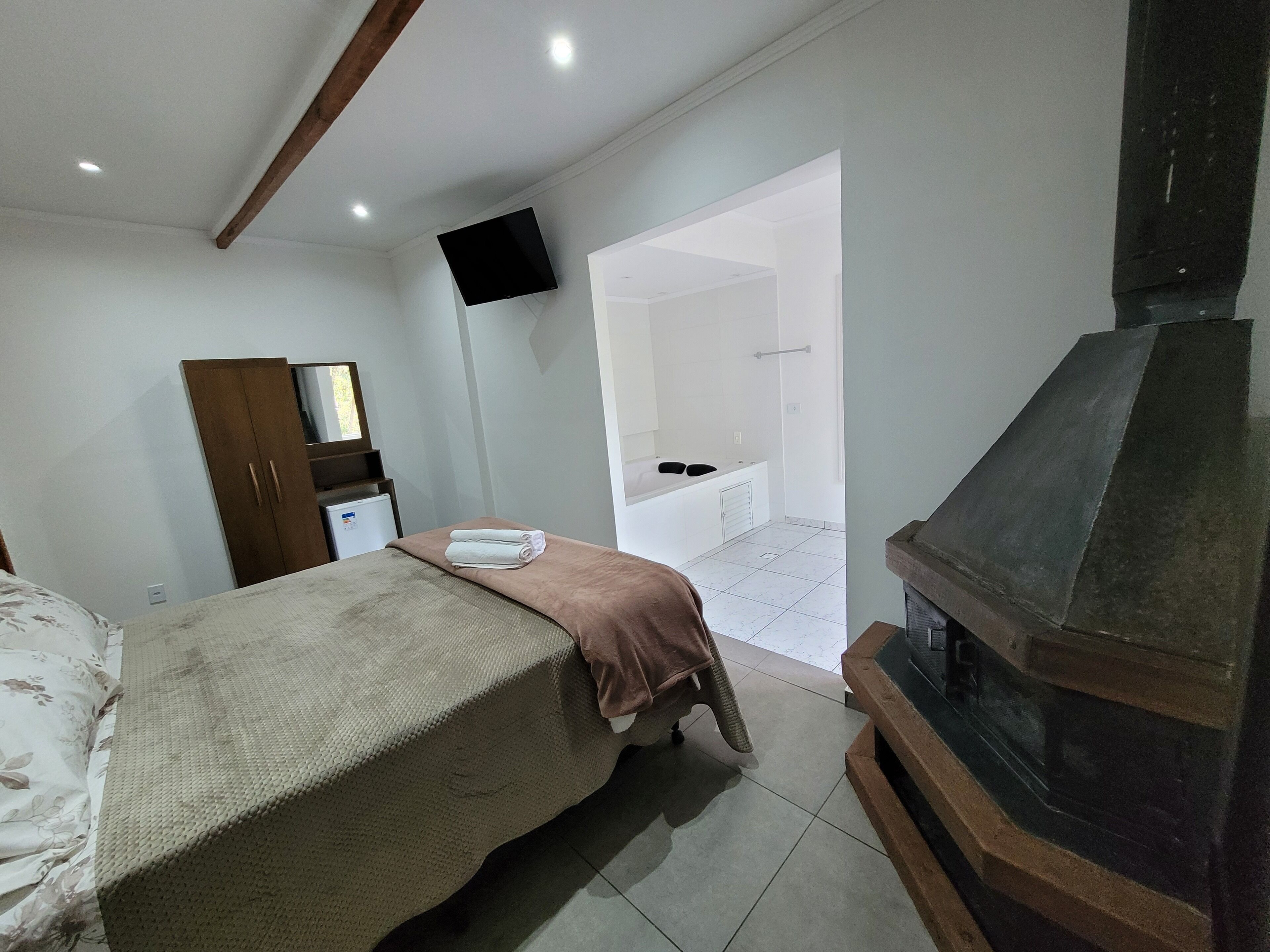 A bedroom with a bed, a wooden wardrobe, a flat-screen TV, a fireplace, and a bathroom visible through an open door.