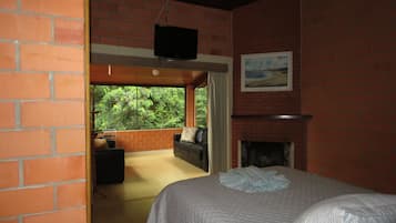 A bedroom with a bed, a fireplace, a TV, and a large window with a view of greenery.