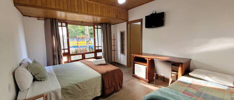Una habitación con dos camas, un escritorio, un televisor y una ventana con vista a un parque infantil.
