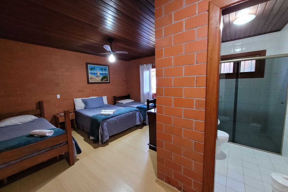 A room with two beds, a ceiling fan, a painting, and a bathroom with a glass shower.