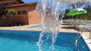 Una piscina con fuente de agua, un patio con sillas de descanso y un edificio al fondo.