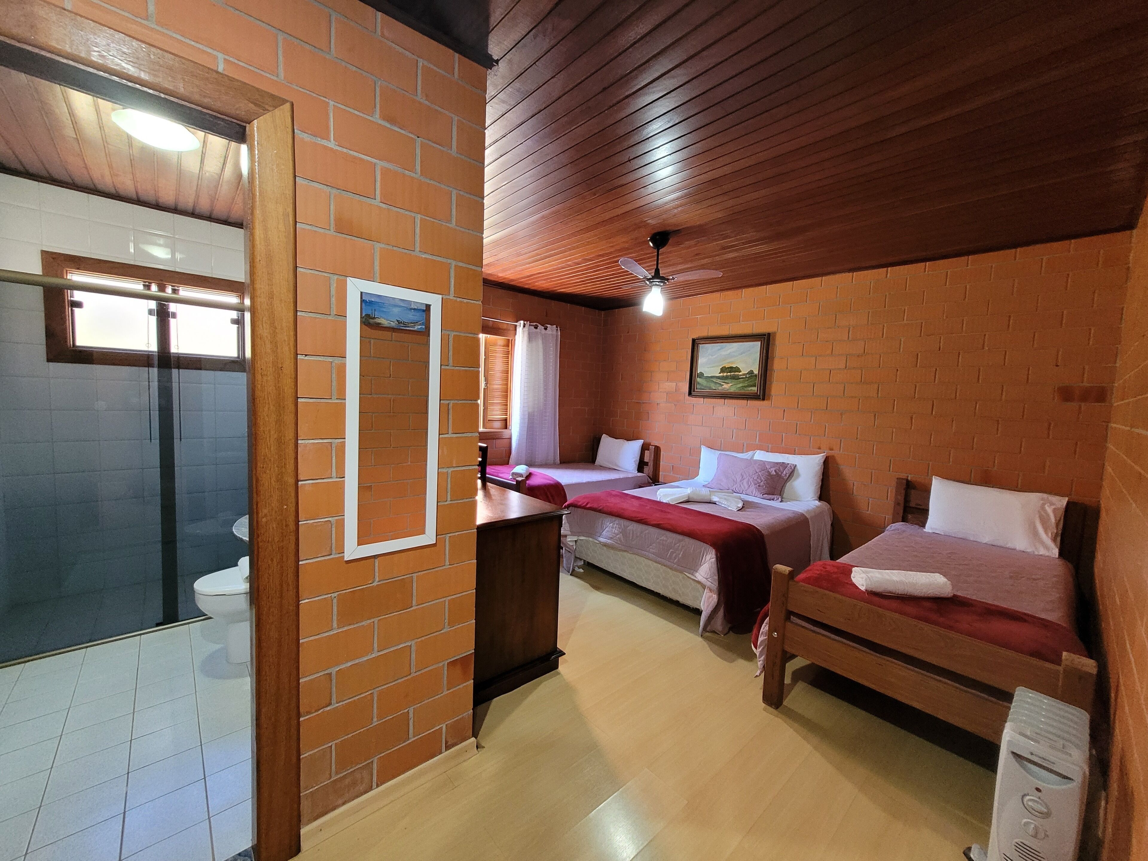 A room with two beds, a wooden ceiling, a brick wall, and a window with a view.